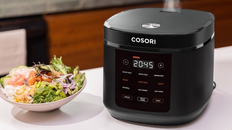 A Cosori rice cooker next to a bowl of rice, salmon, and vegetables
