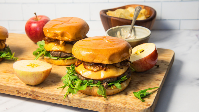 Two caramelized apple burgers on a cutting board with apples