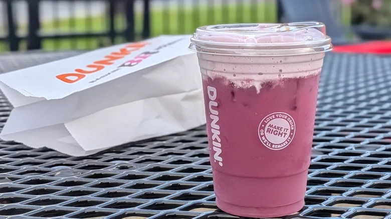 A Dunkin' Berry Batty Daydream Refresher sits on an outdoor table with a Dunkin' takeout bag in the background.