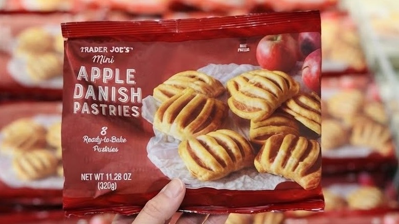 A person holding a package of Trader Joe's Mini Apple Danish Pastries in front of a product display in a store
