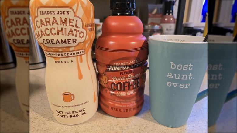 A carton of Trader Joe's Caramel Macchiato Creamer and Pumpkin Spice-Flavored Cold Brew next to a coffee mug
