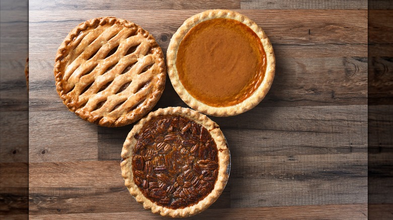 Whole apple, pumpkin, and pecan pies sitting on a wooden table