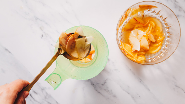 Ladling fruit into a pitcher beside bowl of sangria