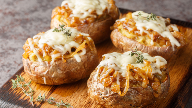 Four French onion-inspired baked potatoes on a wooden board