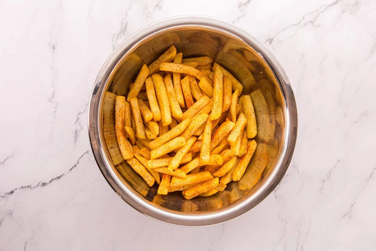 Hot fries in a stainless steel bowl, tossed until every fry is evenly coated in smoky nacho fry seasoning.