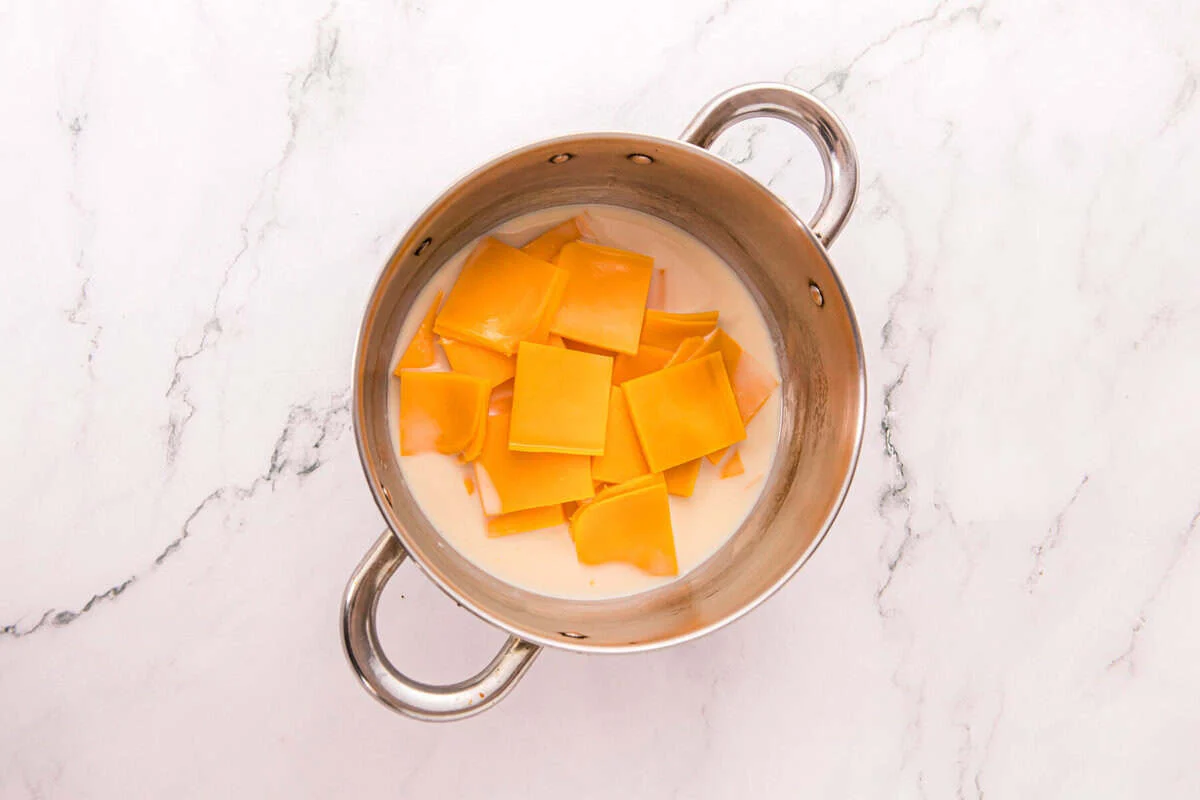Slices of American cheese and evaporated milk in a small stainless steel saucepan, ready to melt into nacho cheese.