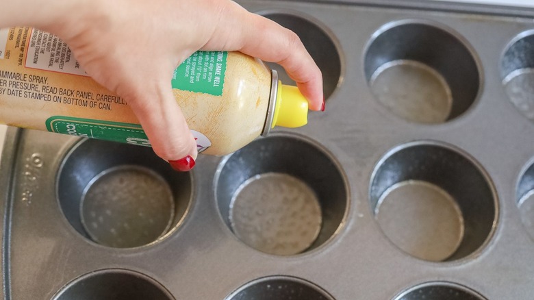 Hand spraying muffin pan with cooking spray
