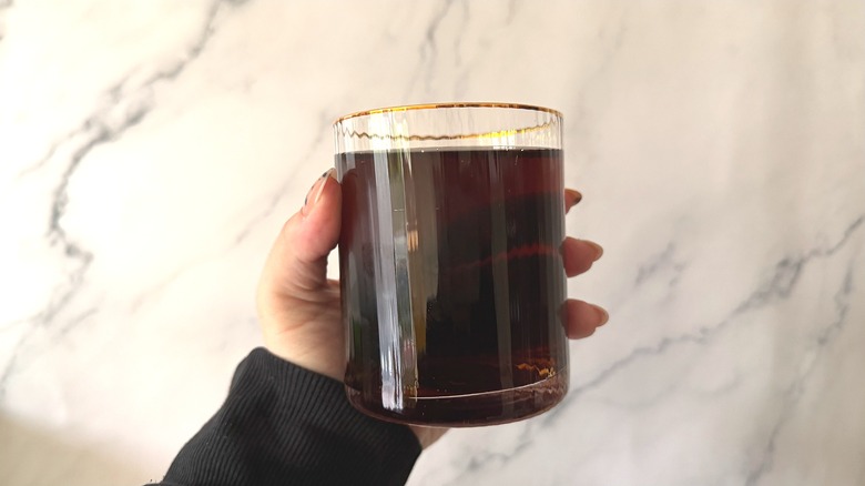 Hand holding gold-rimmed glass of Pepsi Vanilla & Cream against marble background