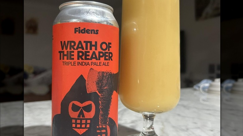 An orange can of Fidens Wrath of the Reaper triple India pale ale featuring a cartoon image of the Grim Reaper holding an ax next to a glass full of an opaque creamy yellow liquid.