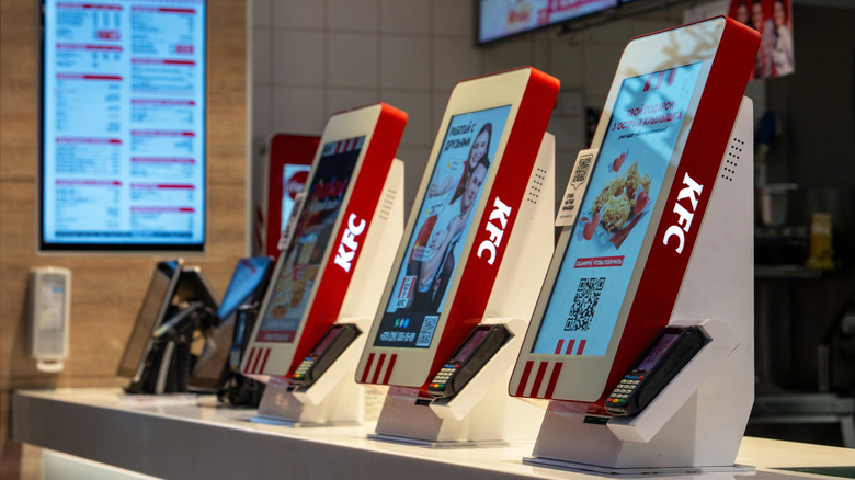 Row of touchscreen ordering kiosks on a counter at KFC