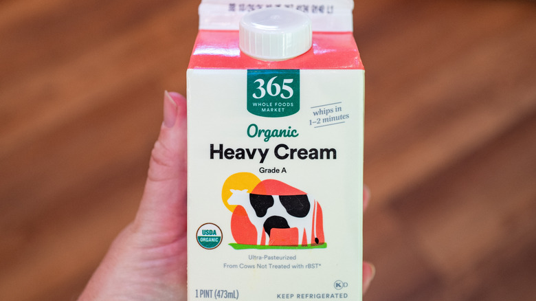 A pint of 365 Whole Foods Organic Heavy Cream held in a person's hand.