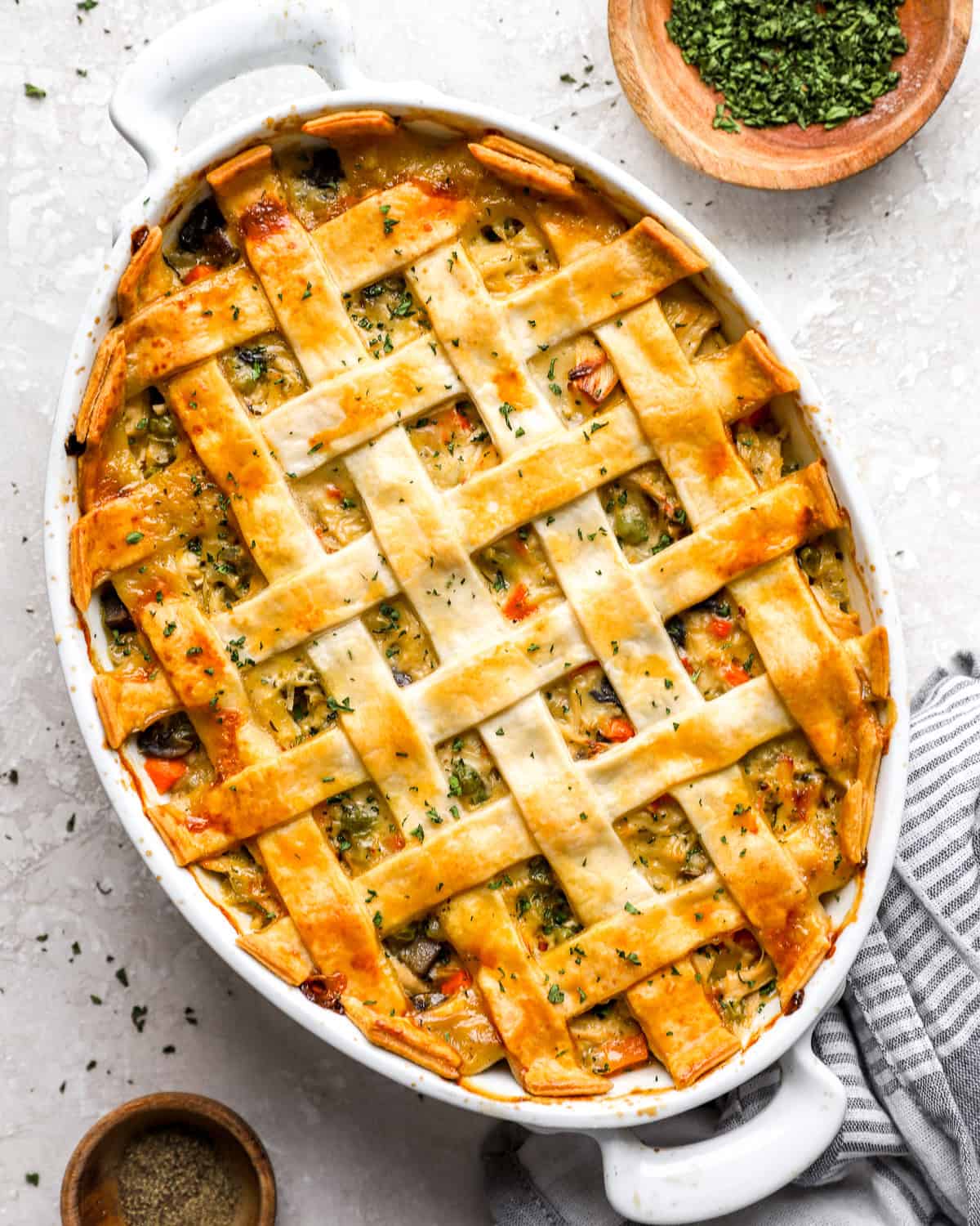 Overhead view of chicken pot pie casserole with a golden lattice pie crust in a white oval baking dish, topped with chopped parsley.