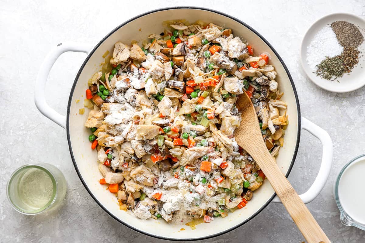Flour sprinkled over the chicken, mushrooms, peas, and veggies in a skillet for chicken pot pie filling.