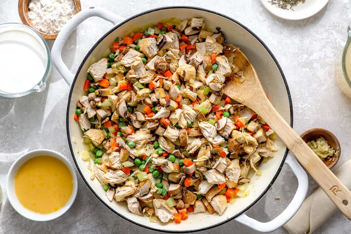 Shredded cooked chicken, mushrooms, and peas added to sautéed carrots, celery, and onion in a skillet.