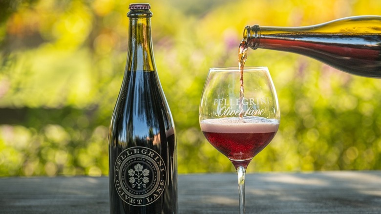 a hand pouring glass of sparkling red wine into a glass