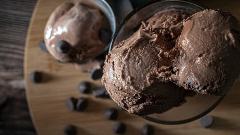 Chocolate ice cream scoops in a glass bowl on a wooden cutting board with chocolate chips