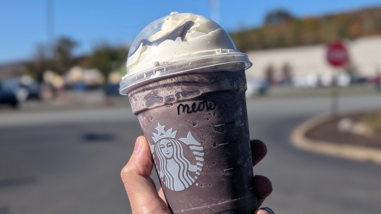A hand holding a Starbucks Black Cat Frappuccino outside with 