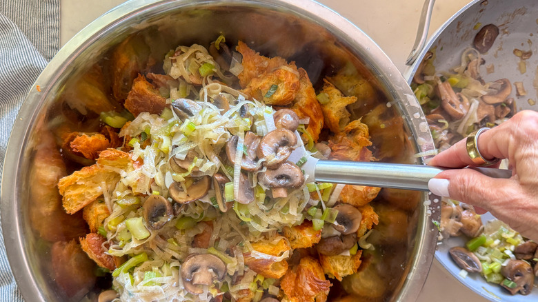 hand adding mushroom mixture to bowl