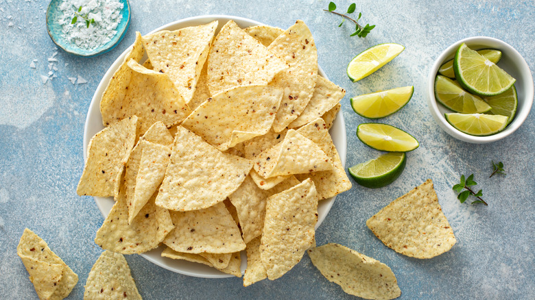 Tortilla chips spilling from bowl, next to bowl of lime wedges