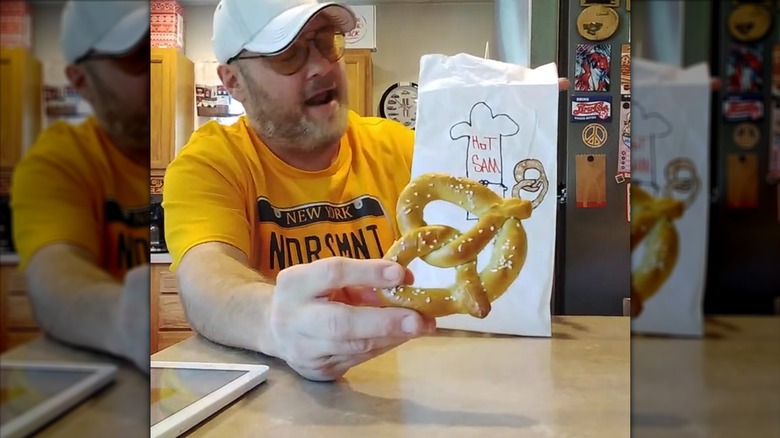 Man holding a Hot Sam pretzel in front of a white paper bag with the logo