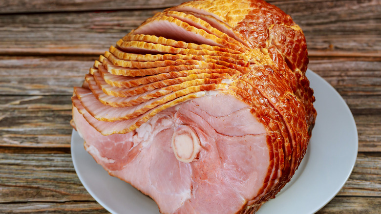 A thinly-sliced cooked ham on a white plate, resting on a wooden table