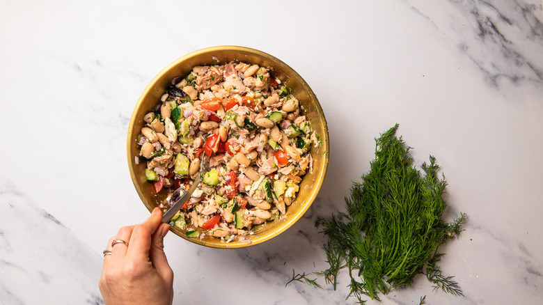 Hand tossing salad in bowl