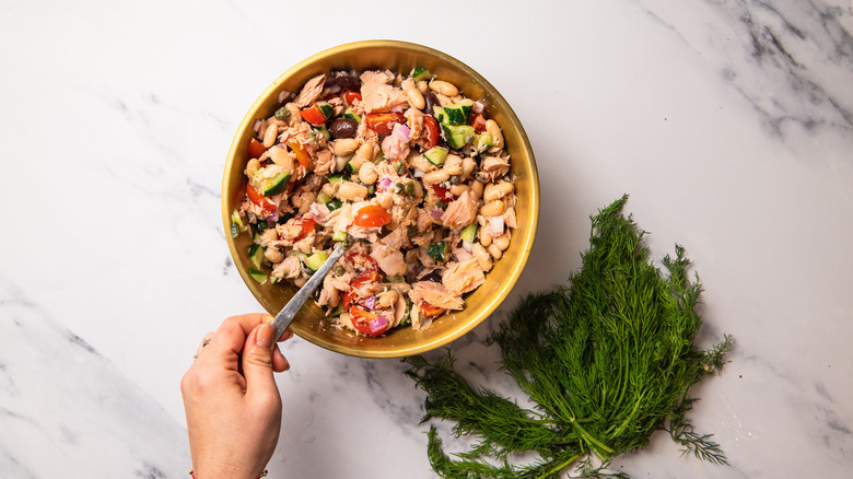 Hand tossing salad in bowl
