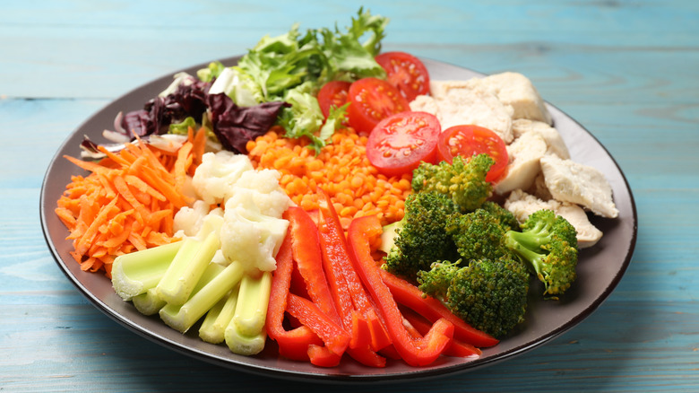 Cooked chicken breast served with an array of colorful egetables and lentils