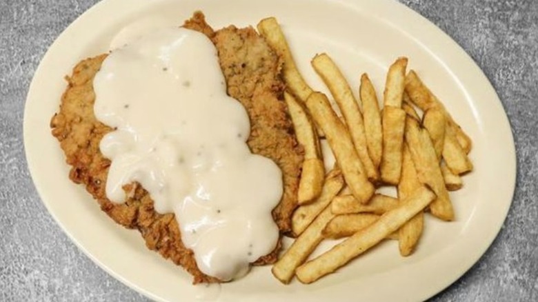 Top-down shot of chicken fried steak topped with gravy and fries on white plate