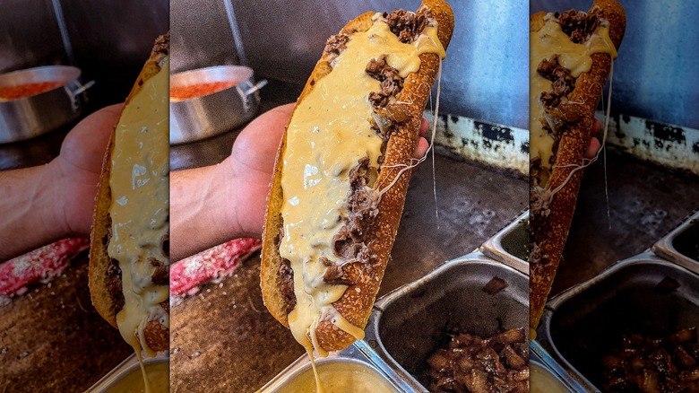 Hand holding cheesesteak loaded with cheese sauce over grill