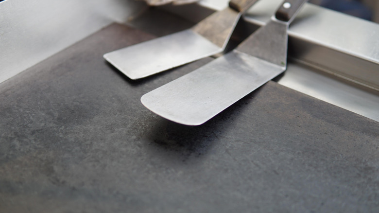 A clean, professional flat-top griddle with two long, wooden handled spatulas on top of it
