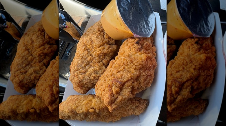 Three chicken strips from Costco inside white paper boat container next to small plastic cup of dipping sauce