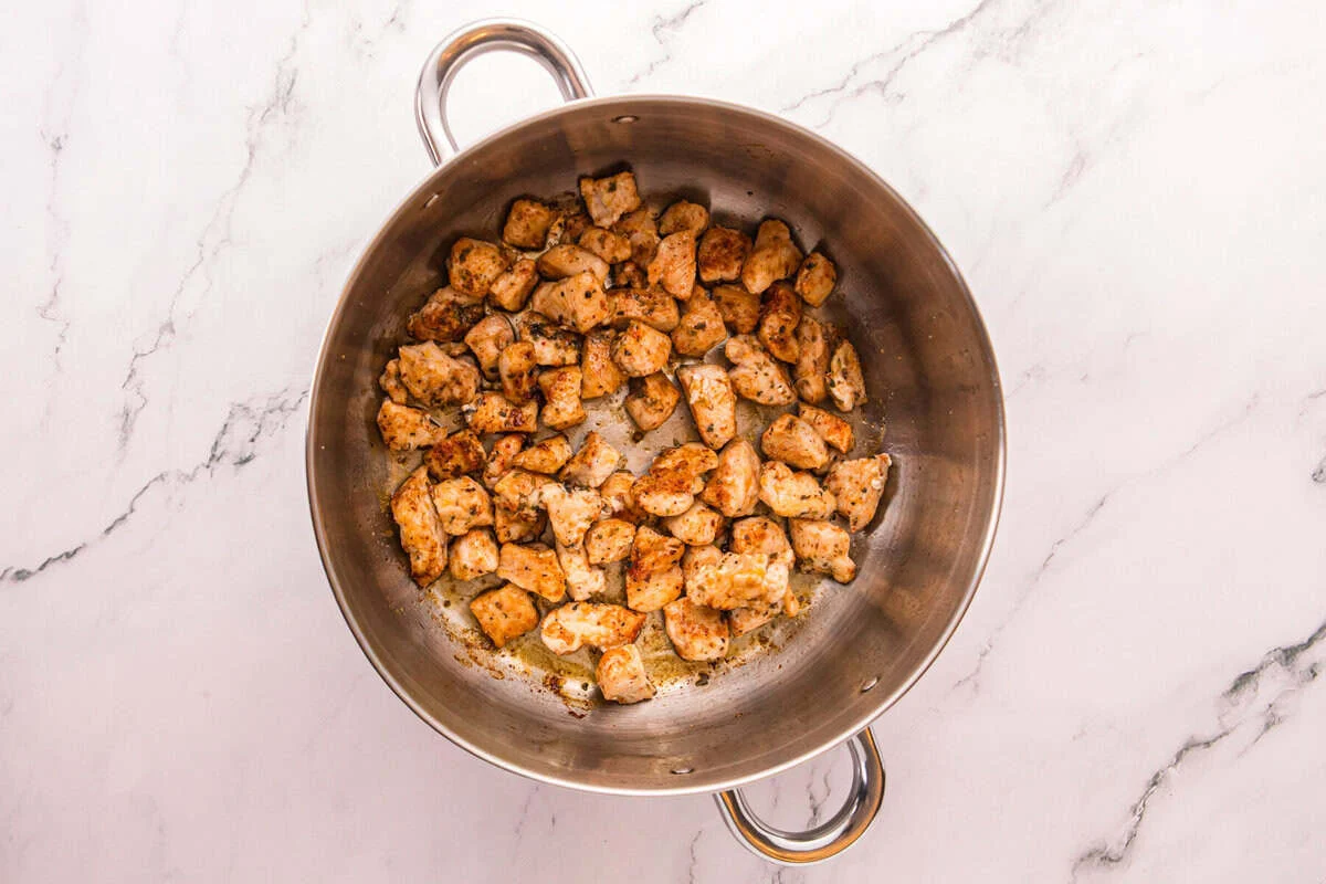 Seasoned chicken pieces browned in a large stainless steel pot.