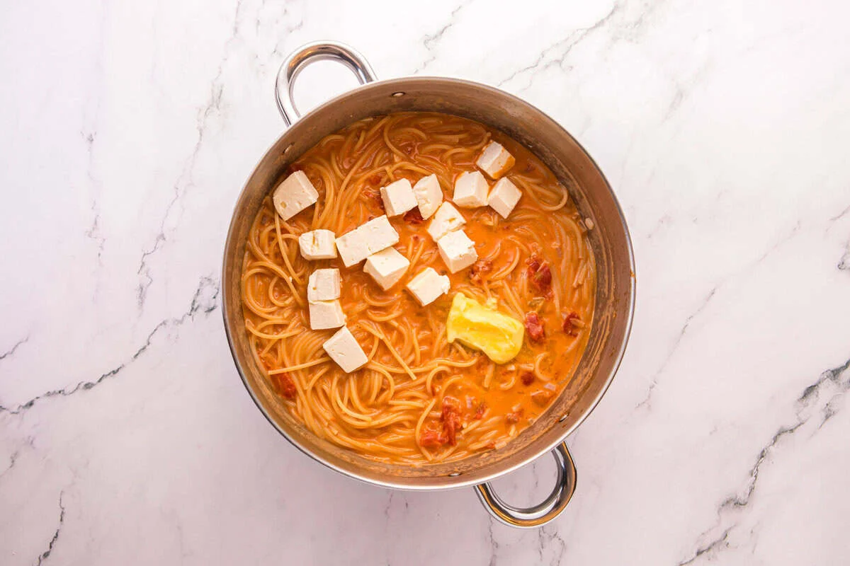 Cubes of cream cheese and butter added to cooked spaghetti in a creamy sauce.