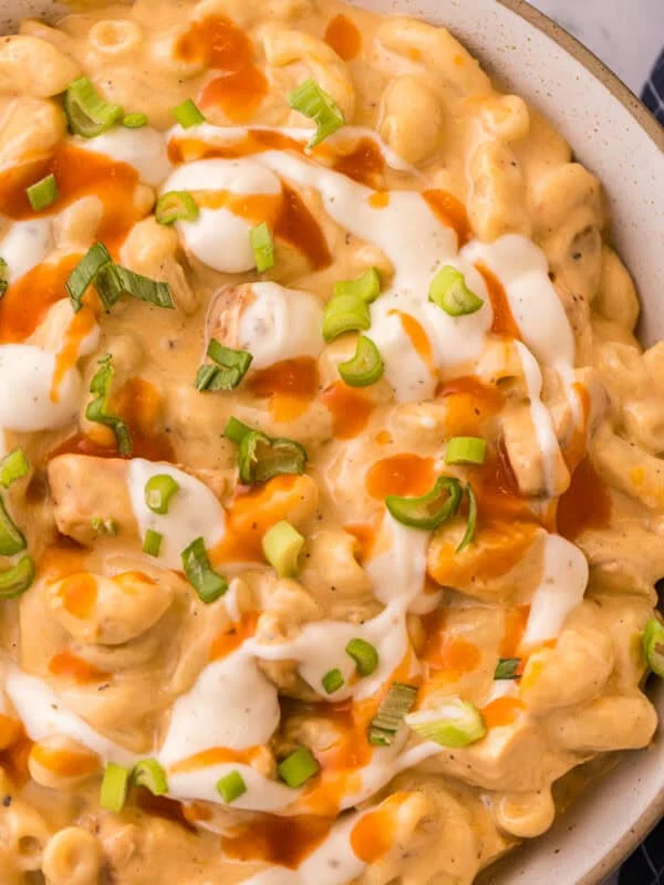 Overhead view of a bowl of one-pot buffalo chicken mac and cheese topped with a drizzle of ranch, buffalo sauce, and sliced green onions.