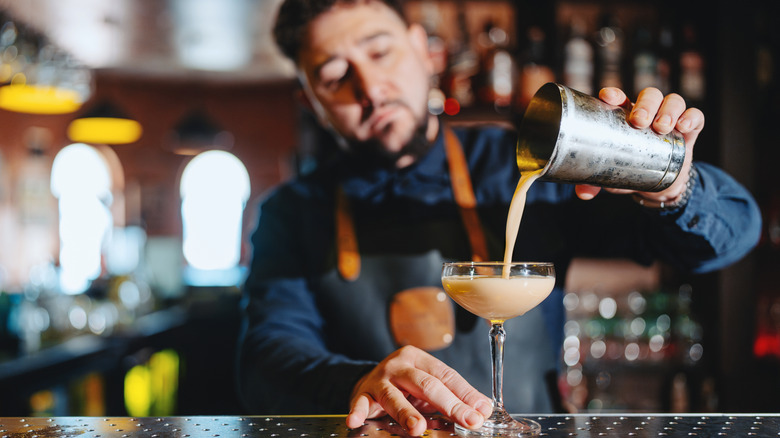 A bartender pouring a cocktail into a glass from a shaker