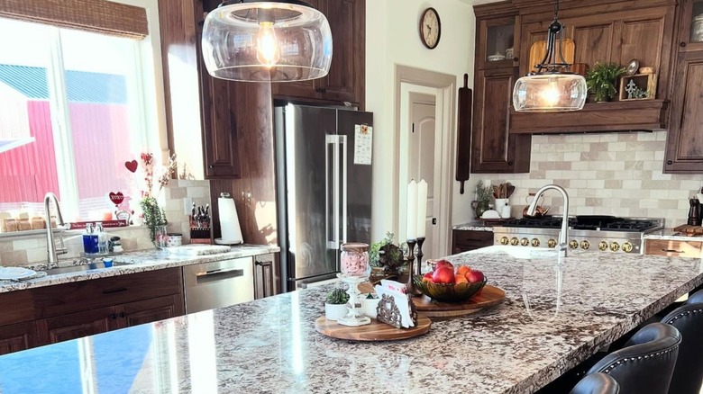 A kitchen with Bianco Antico granite countertops and kitchen island and warm espresso-stained wood cabinets