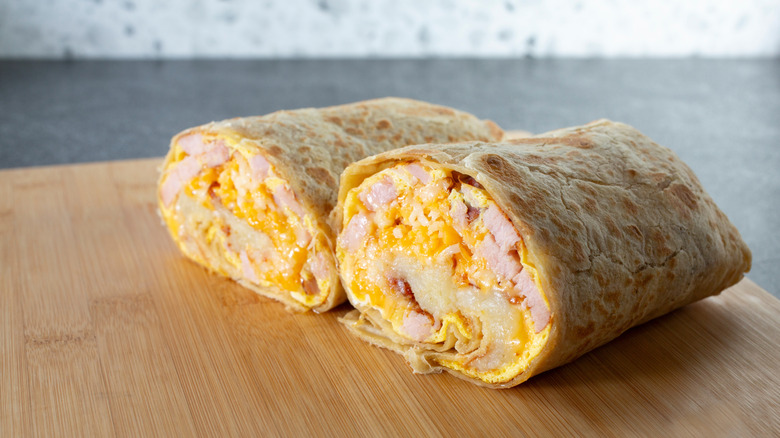 breakfast egg burrito cut in half to show cross section on wooden board