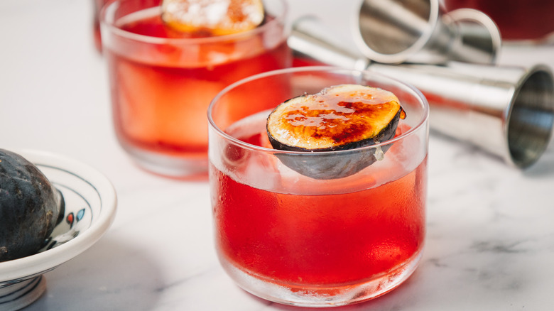 Close up on two cocktails with jiggers and whole fig